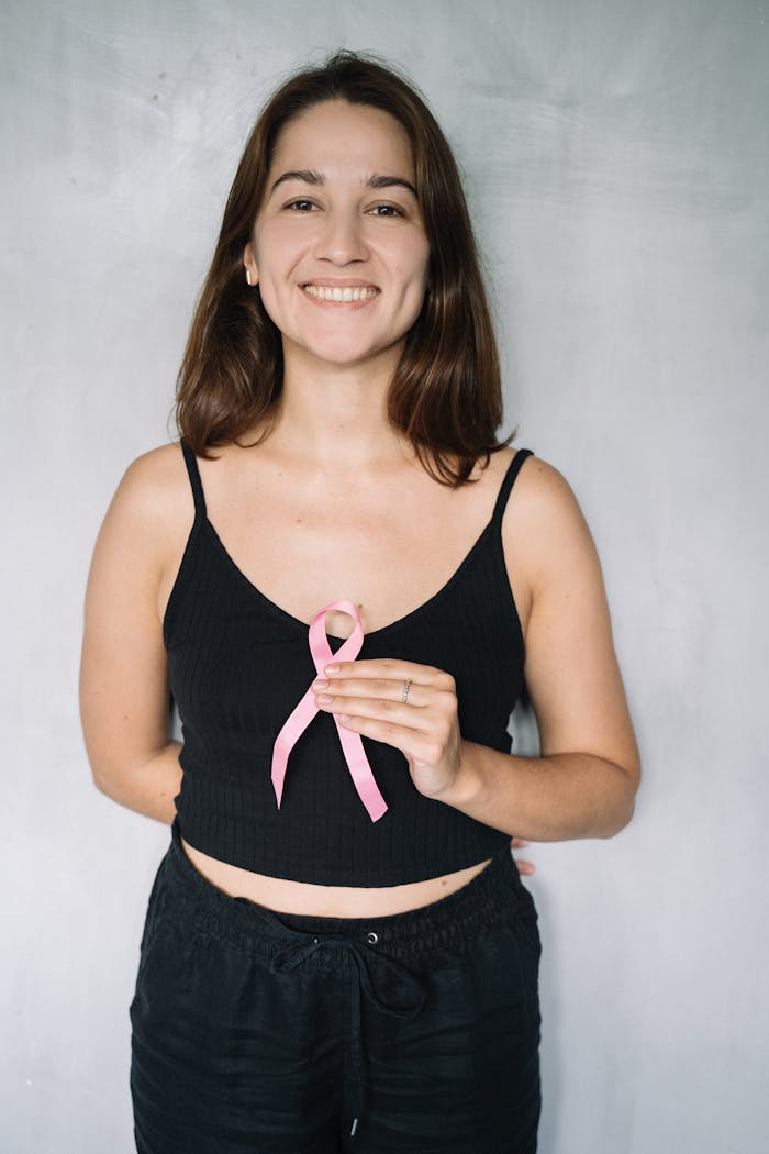 Portrait of a smiling woman holding a pink ribbon to support breast cancer awareness.